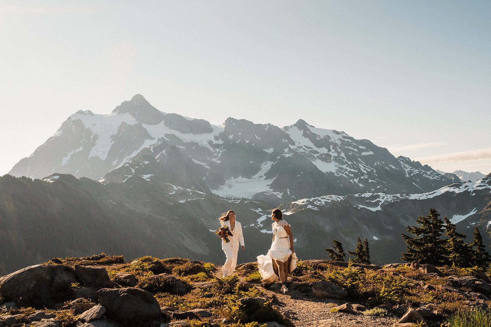 Two brides run along a mountain trail at their wedding in a national park