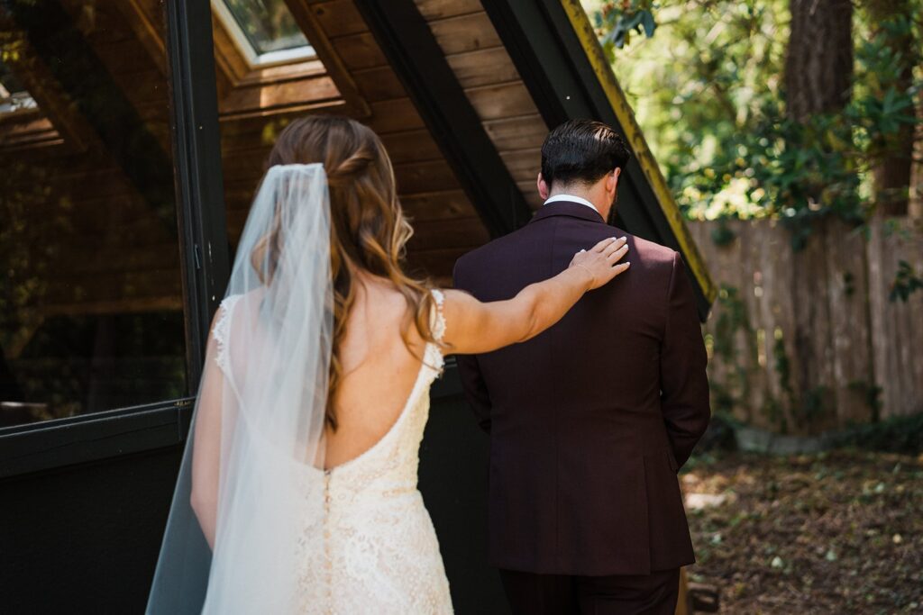 Bride taps groom on the shoulder for their wedding first look outside an A-frame cabin