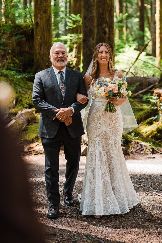 Brides walks down the aisle on her father's arm at her intimate cabin wedding in the forest 