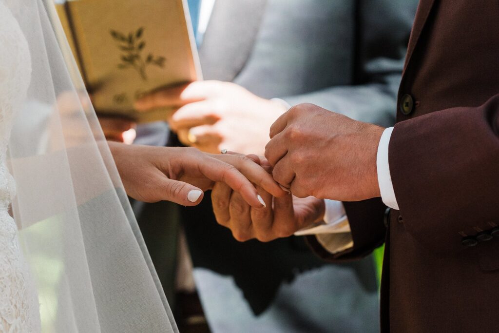 Groom slips a ring onto bride's finger during their forest wedding ceremony in Washington