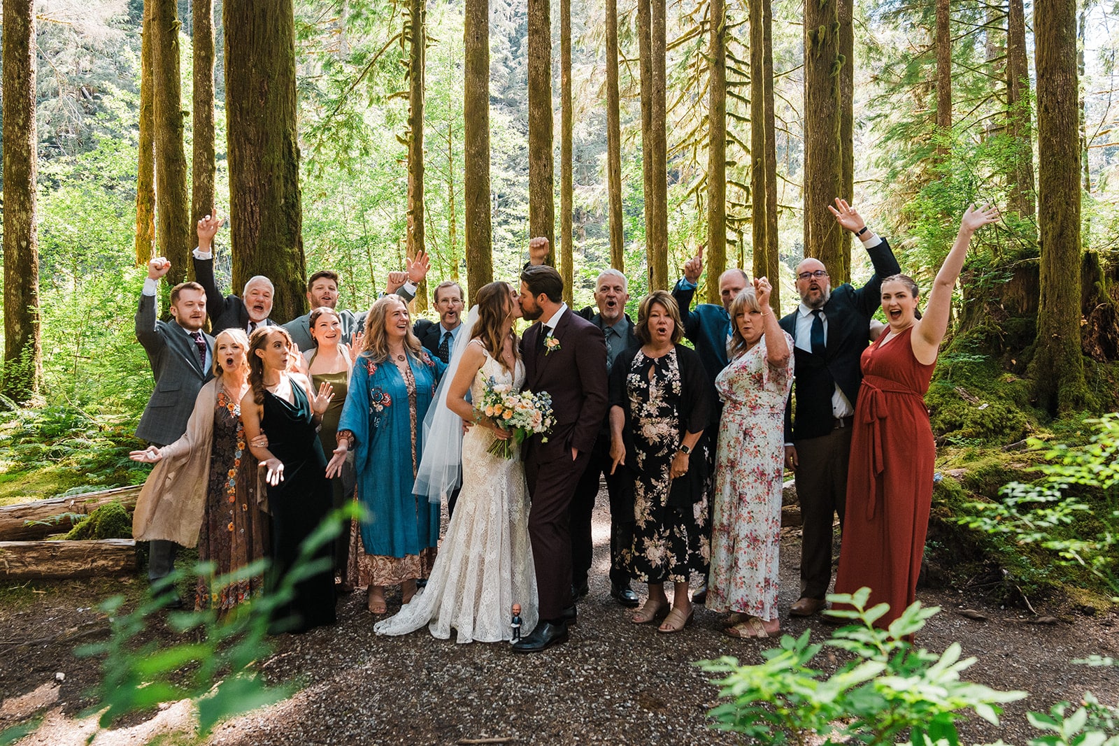 Bride and groom kiss while their loved ones cheer at their micro wedding in the forest 