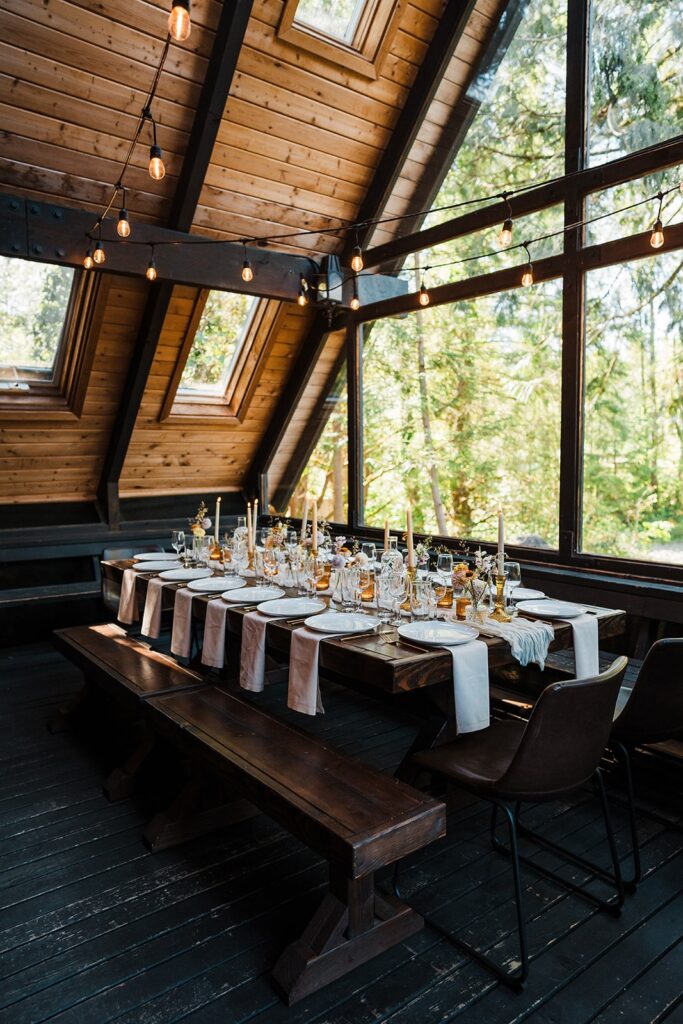 Wood table in an A-frame cabin atrium set with with plates and napkins with string lights hanging above