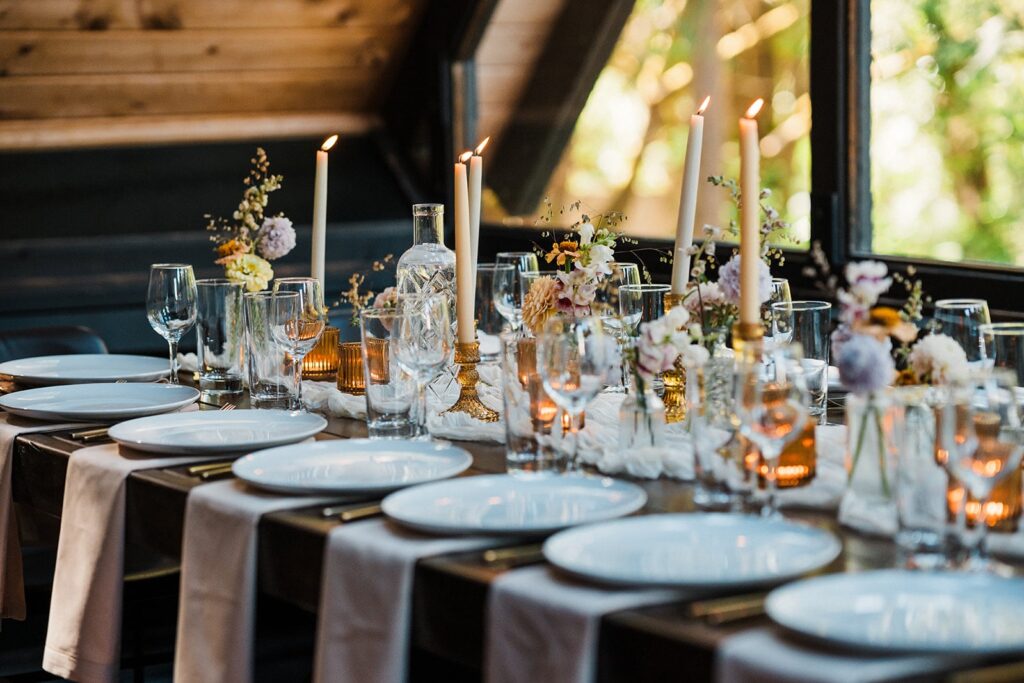 White plates and napkins line a wood table at an intimate cabin wedding reception