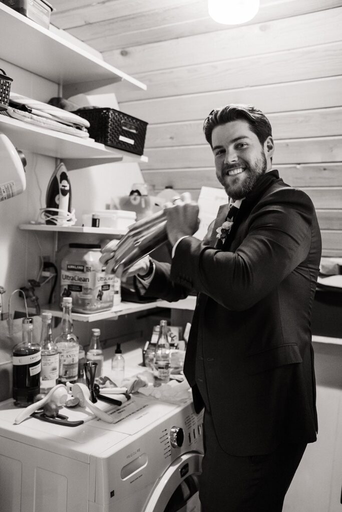 Groom shakes a cocktail shaker in a cabin kitchen 