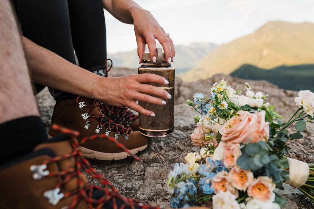 Bride unscrews her water bottle cap while sitting on a mountain trail in Snoqualmie Valley