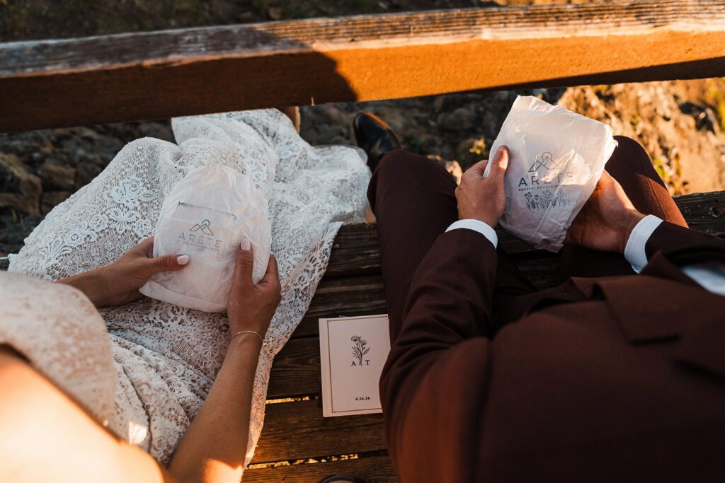 Bride and groom hold pastry bags while sitting on the edge of a fire lookout near Mount Rainier