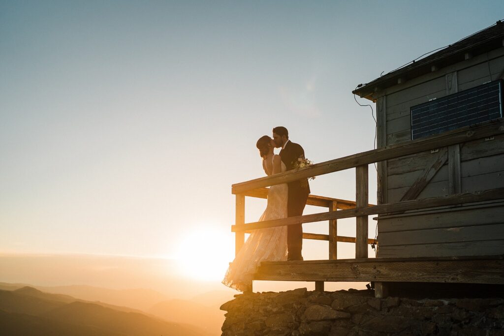 Bride and groom kiss on the deck of a fire lookout at sunset 