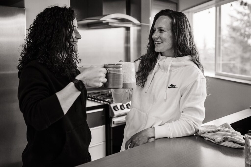 Two women drink coffee in the kitchen of their Airbnb before their LGBTQ elopement during pride month