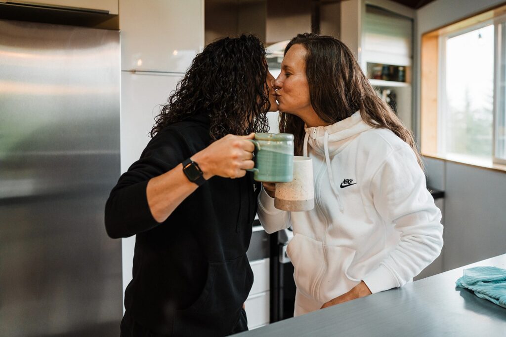 Women kiss in the kitchen on the morning of their LGBTQ wedding.