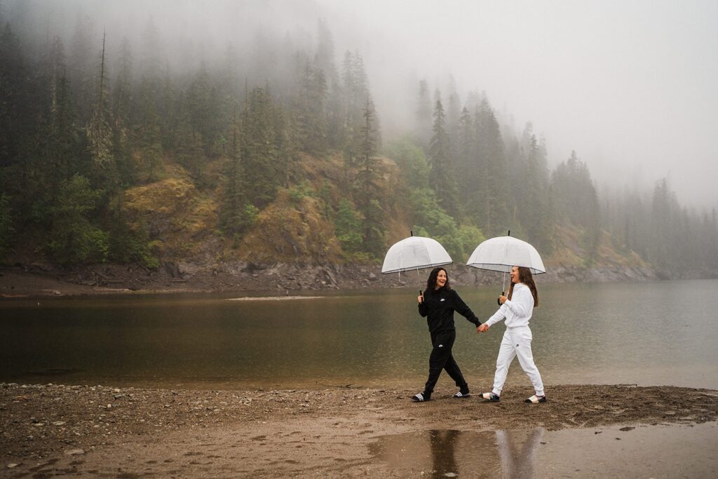 Women hold hands while walking around an alpine lake during their sunrise LGBTQ wedding in Washington