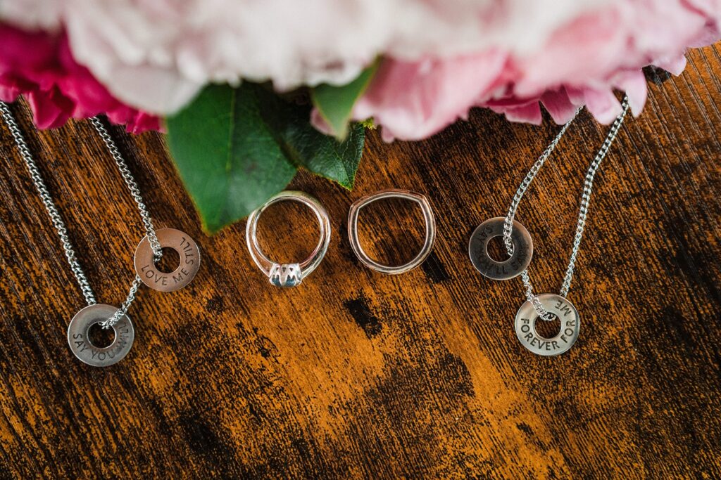 Matching silver necklaces with wedding bands and pink flowers