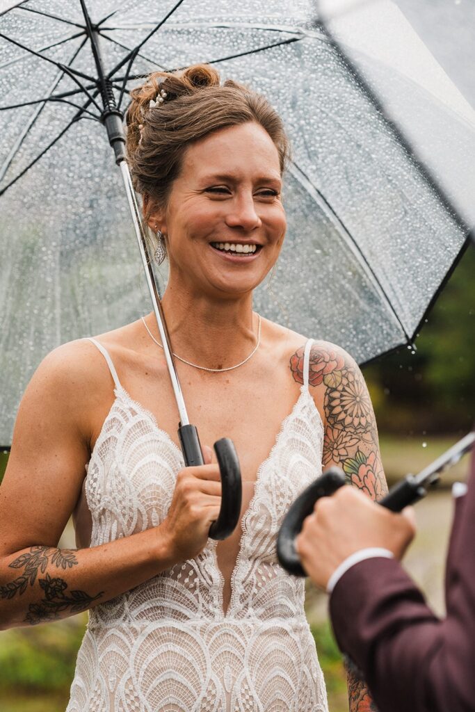 Bride smiles while holding a clear umbrella during her rainy wedding ceremony in Washington