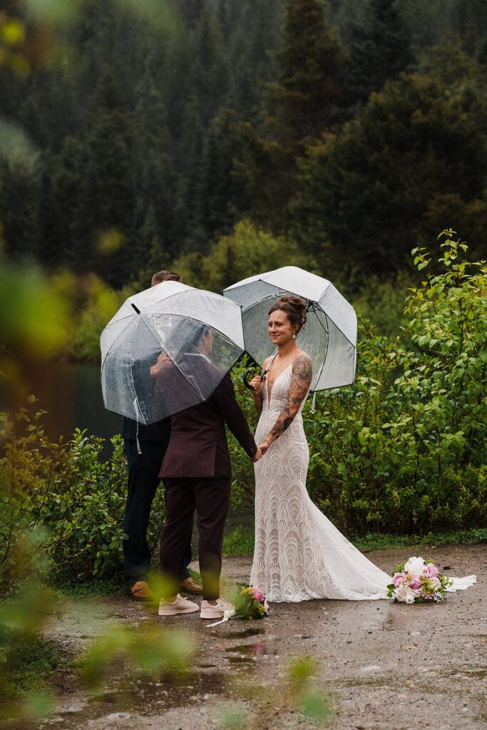 Brides hold hands during their rainy wedding ceremony by an alpine lake in Snoqualmie, WA