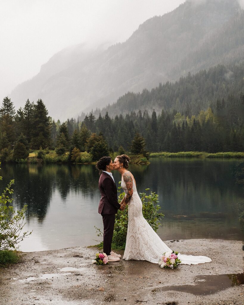 Brides kiss during their LGBTQ elopement ceremony in the rain by an alpine lake