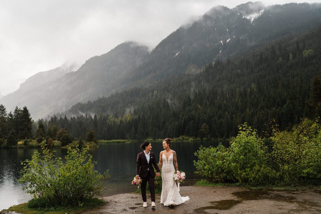 Brides hold hands by an alpine lake after their LGBTQ wedding ceremony in Washington