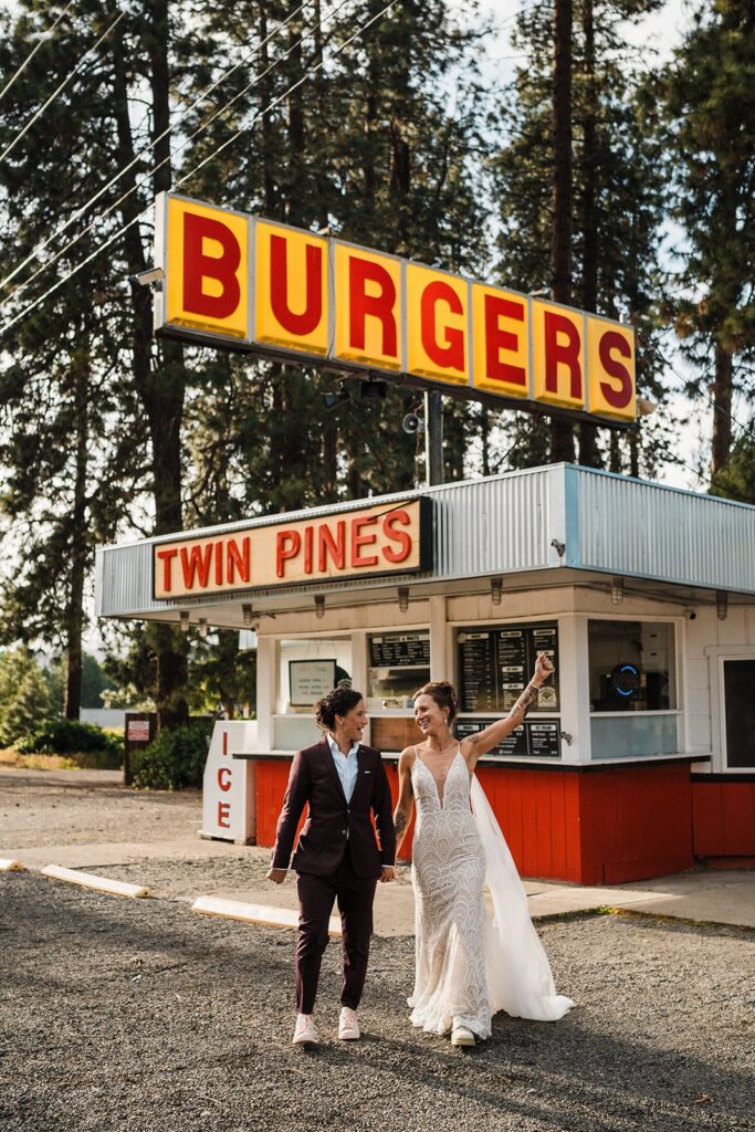 Brides hold hands in front of a burger restaurant at their LGBTQ elopement in Washington