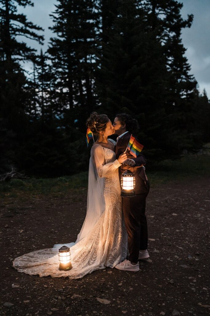 Brides hold pride flags and lanterns during blue hour at their LGBTQ wedding in Washington