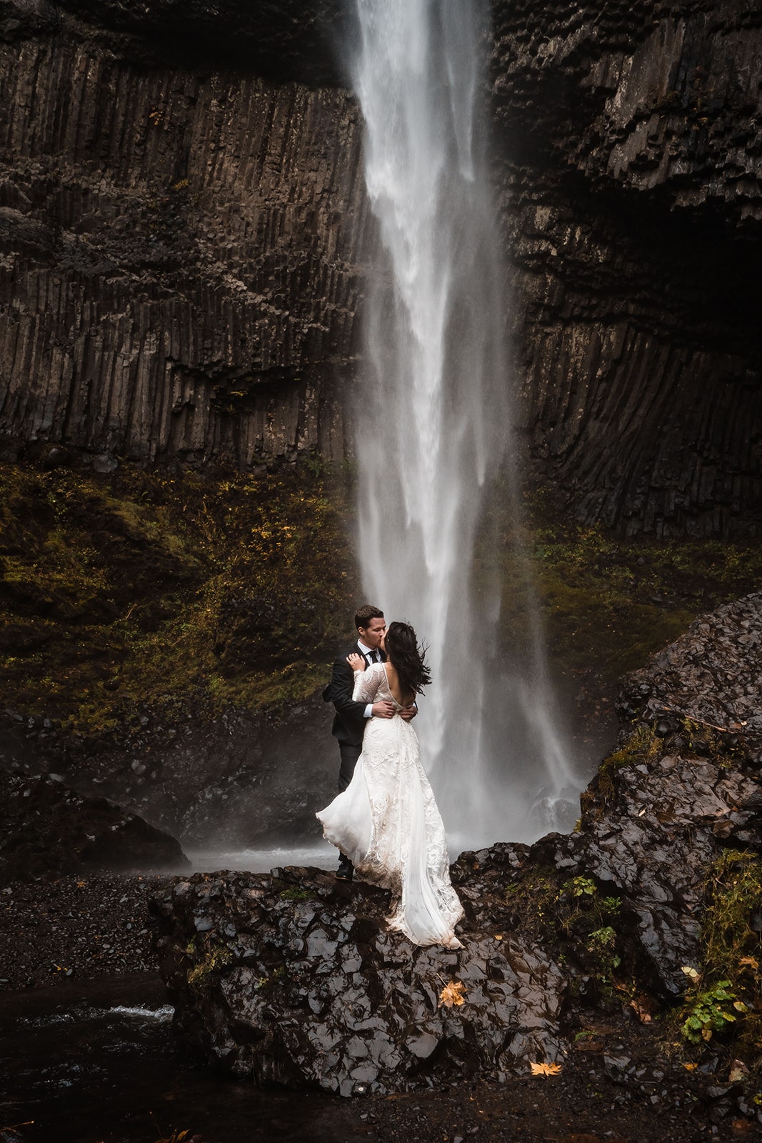 Bride and groom kiss in front of a waterfall at their Oregon micro wedding