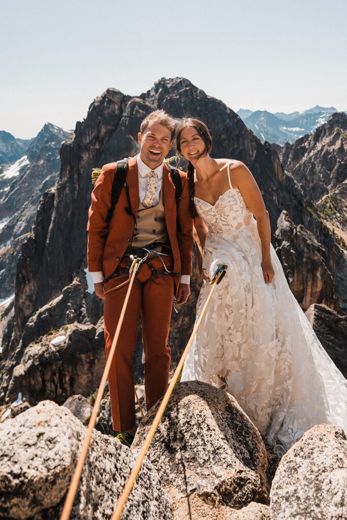 Bride and groom wear climbing gear with their wedding attire while standing on a mountain peak in the North Cascades