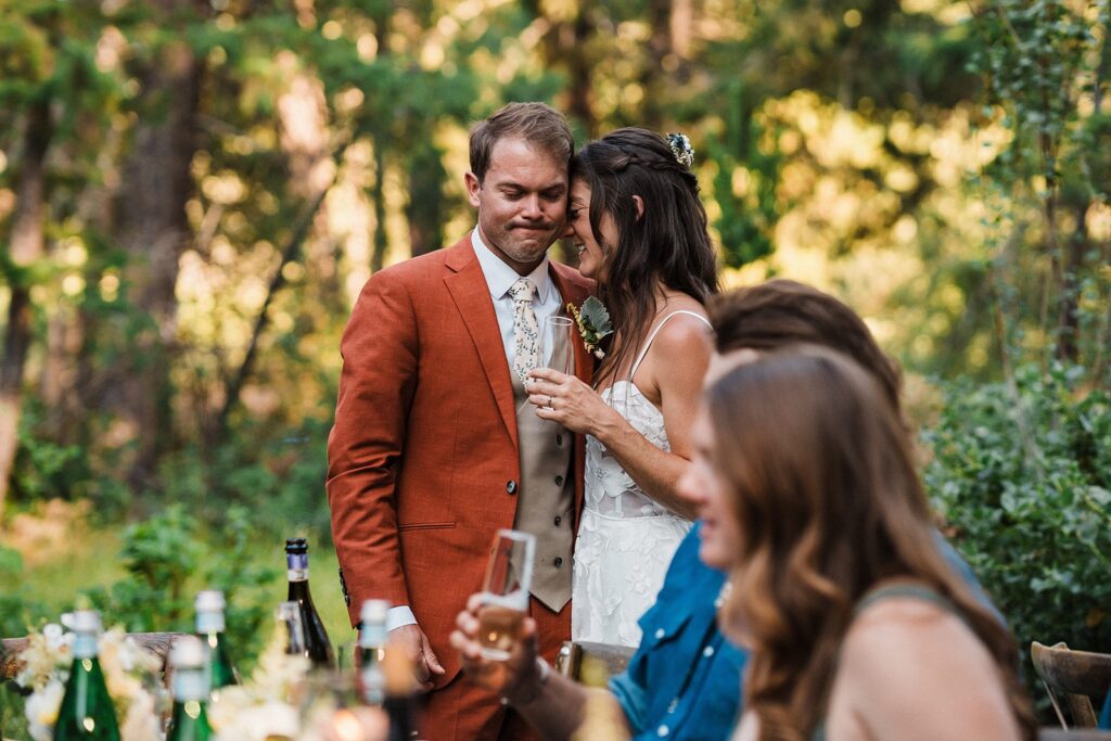 Bride and groom stand at the head of their reception dinner table at Apres Cabin