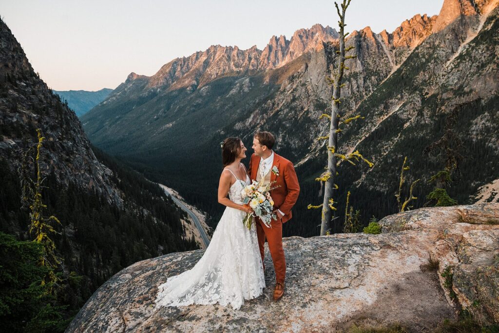 Bride and groom stand on a mountain trail at sunset during their North Cascades elopement