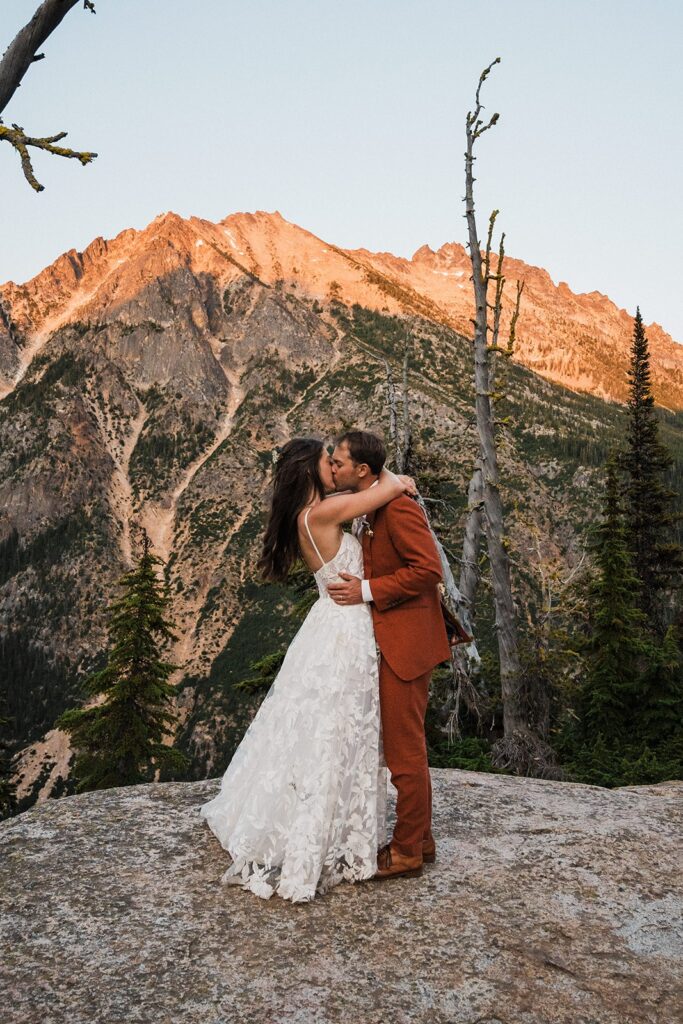 Bride and groom kiss on a mountain trail after their rock climbing elopement