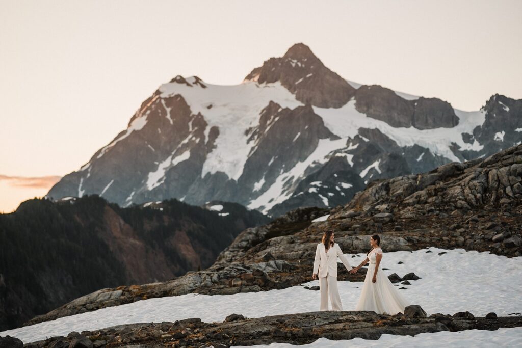 Brides hold hands as they walk across a snowy trail during their elopement at Artist Point 