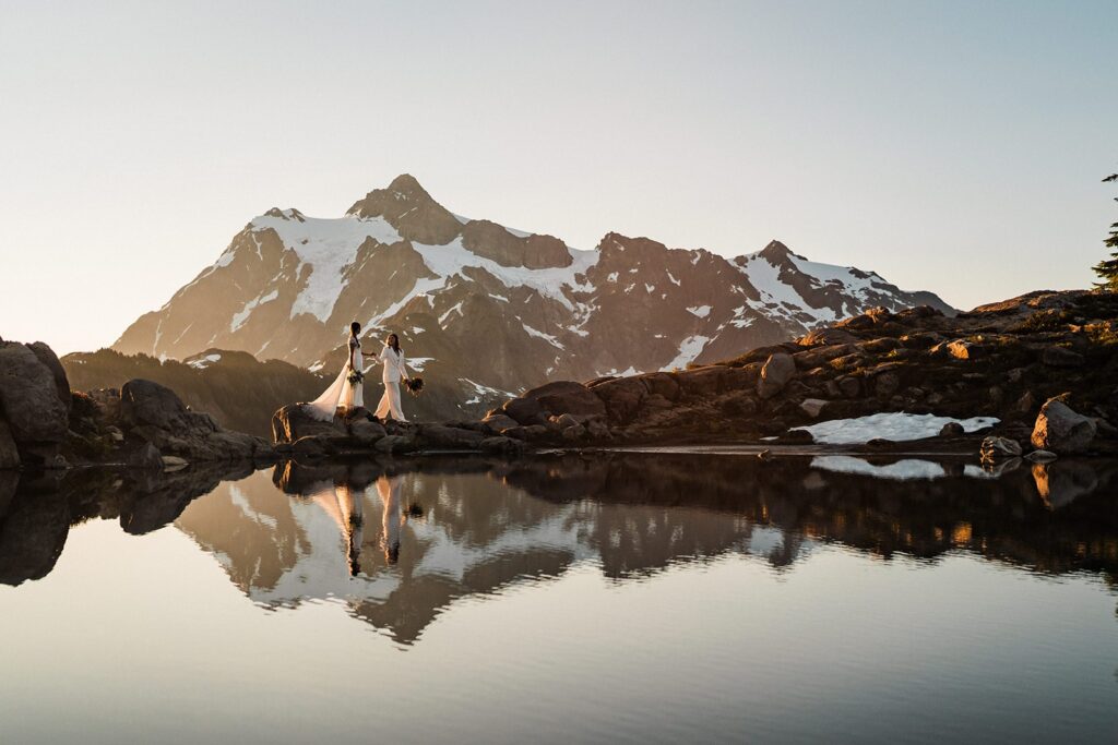 Brides walk along an alpine lake during their sunrise summer elopement at Artist Point 