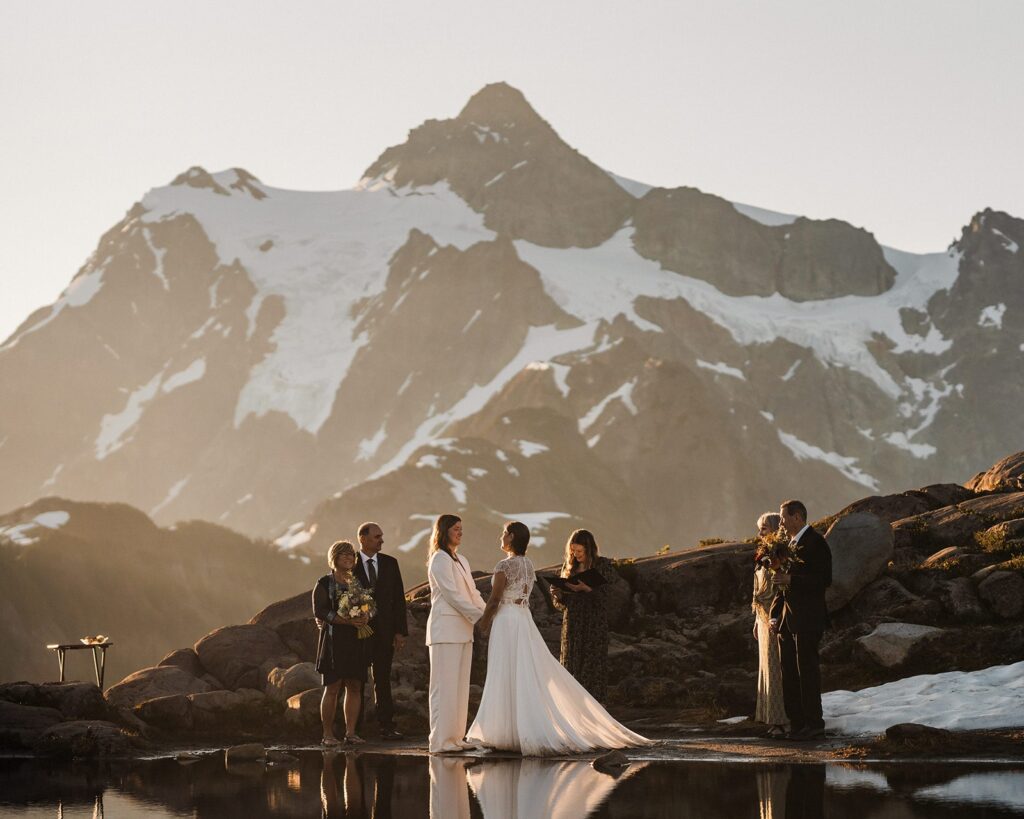 Brides hold hands as their parents look on during their summer sunrise elopement at Artist Point 