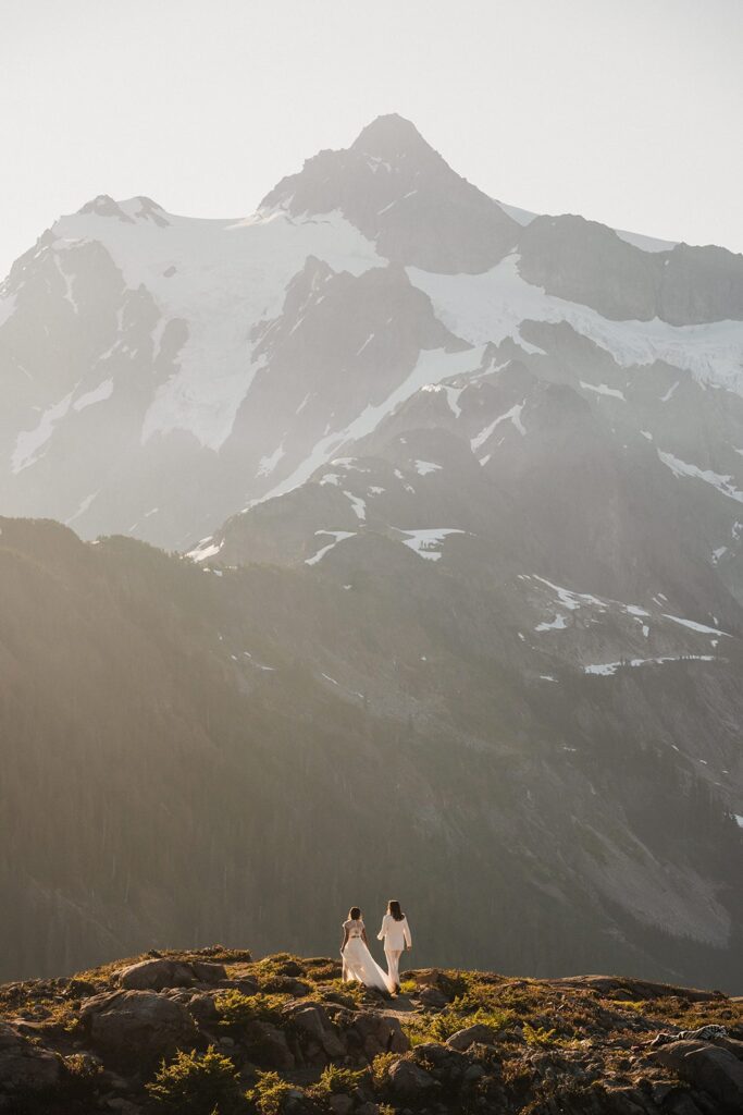 Brides walk across a mountain trail during their summer elopement 