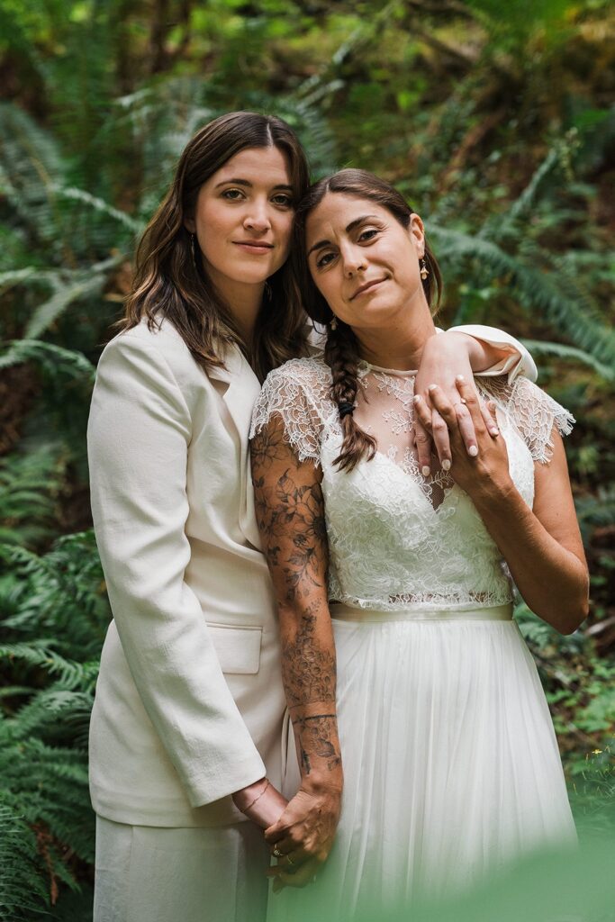 Brides hold hands in the forest during their summer elopement in the North Cascades