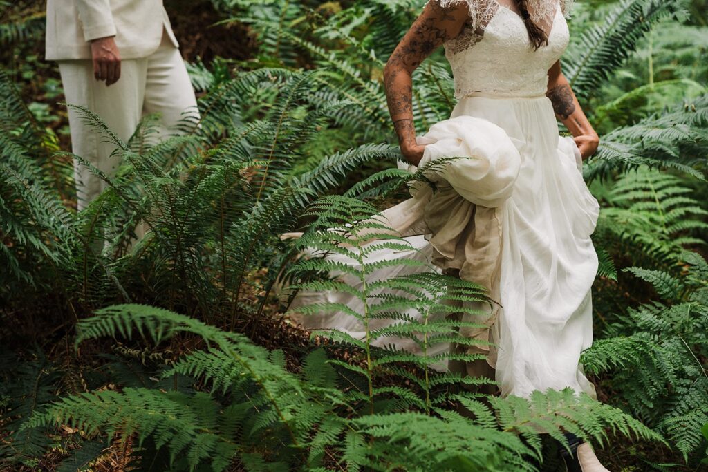 Brides walk through a fern-filled trail in the forest during their summer elopement in the North Cascades 