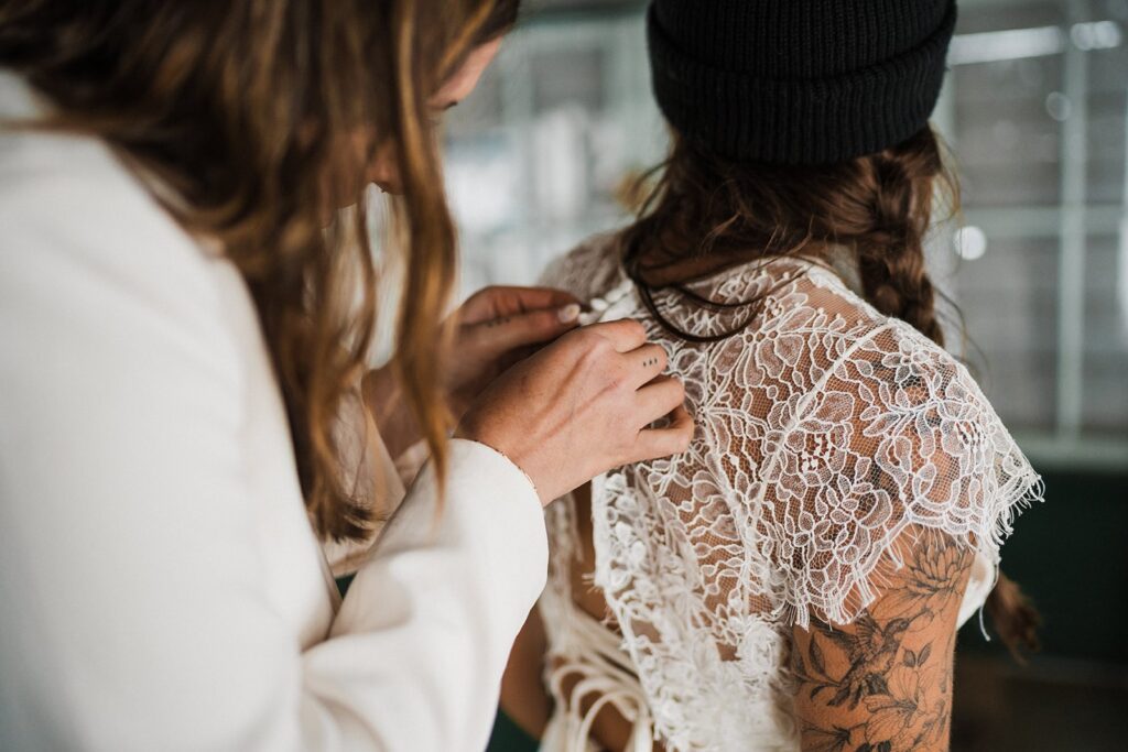 Bride helps other bride button her dress for their elopement in the North Cascades