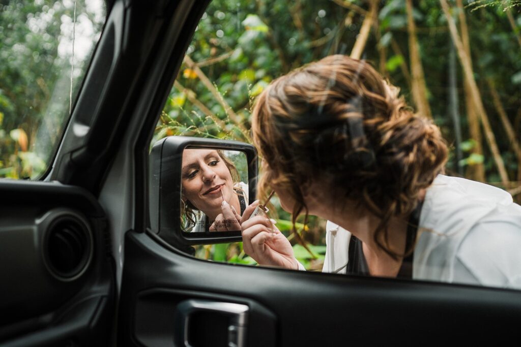 Bride puts on lipstick in car mirror before her elopement in Kauai 