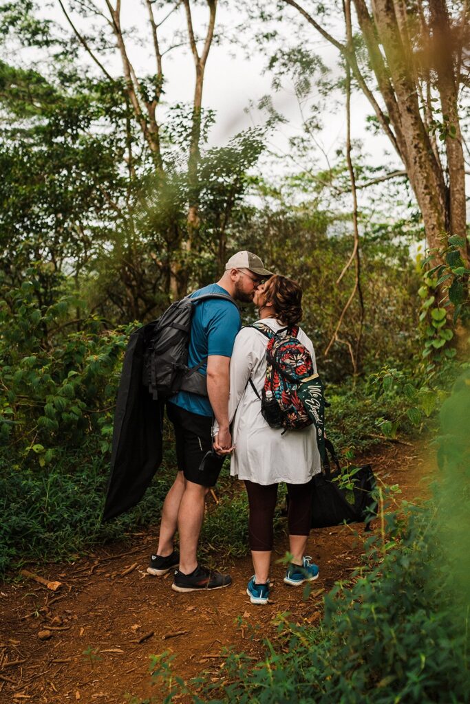 Bride and groom kiss while hiking a rainforest trail to their first look location in Kauai 