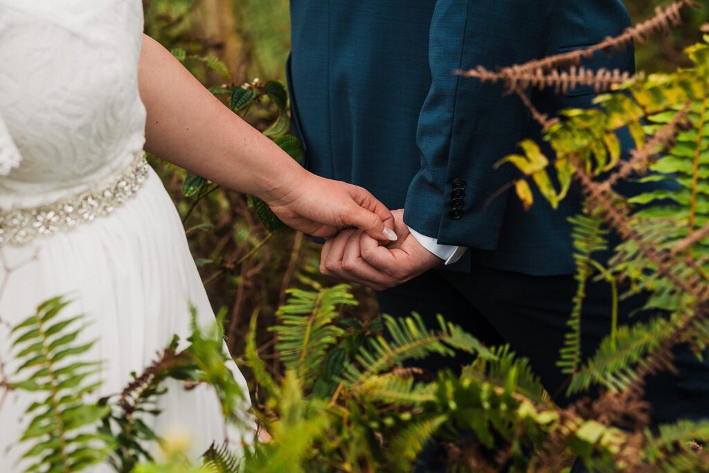 Bride and groom hold hands while walking through a rainforest trail in Kauai 