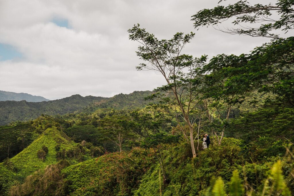 Bride and groom kiss on a rainforest trail surrounded by lush green mountains in Kauai 