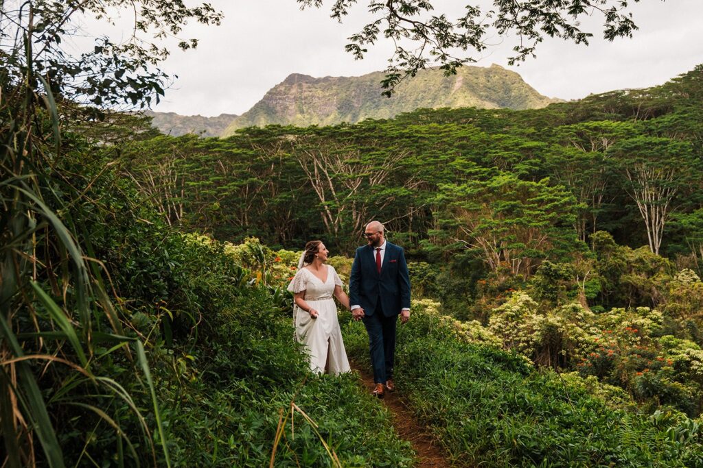 Bride and groom hold hands while walking along a rainforest trail at their elopement in Kauai 