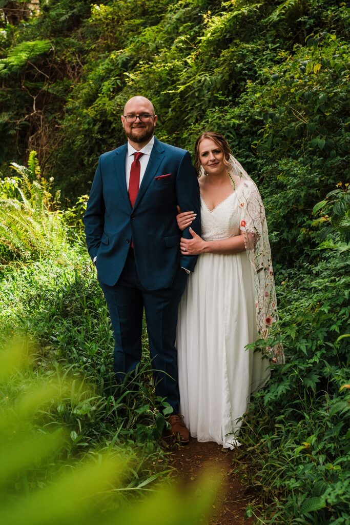 Bride and groom stand on a lush green forest trail at their elopement in Kauai 