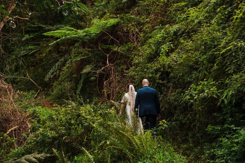 Bride and groom walk along a lush green forest trail at their Kauai Hawaii elopement 