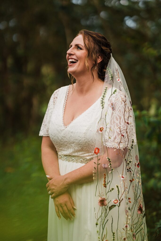 Bride laughs while wearing a white elopement dress with embroidered floral veil 