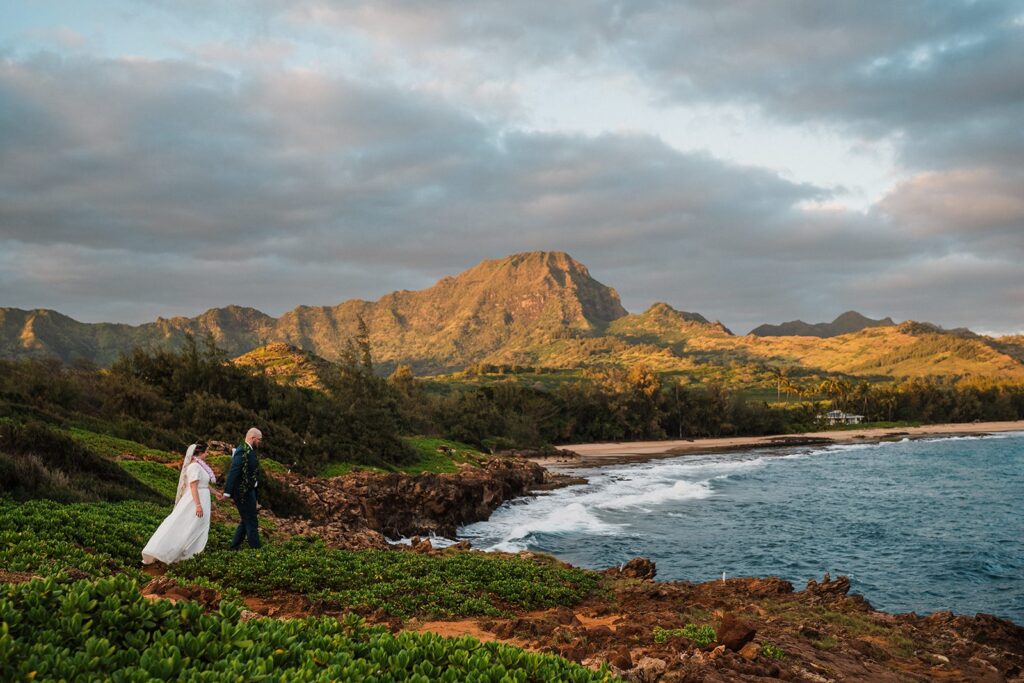 Bride and groom hold hands while walking across the coastal cliffs at their elopement in Kauai 