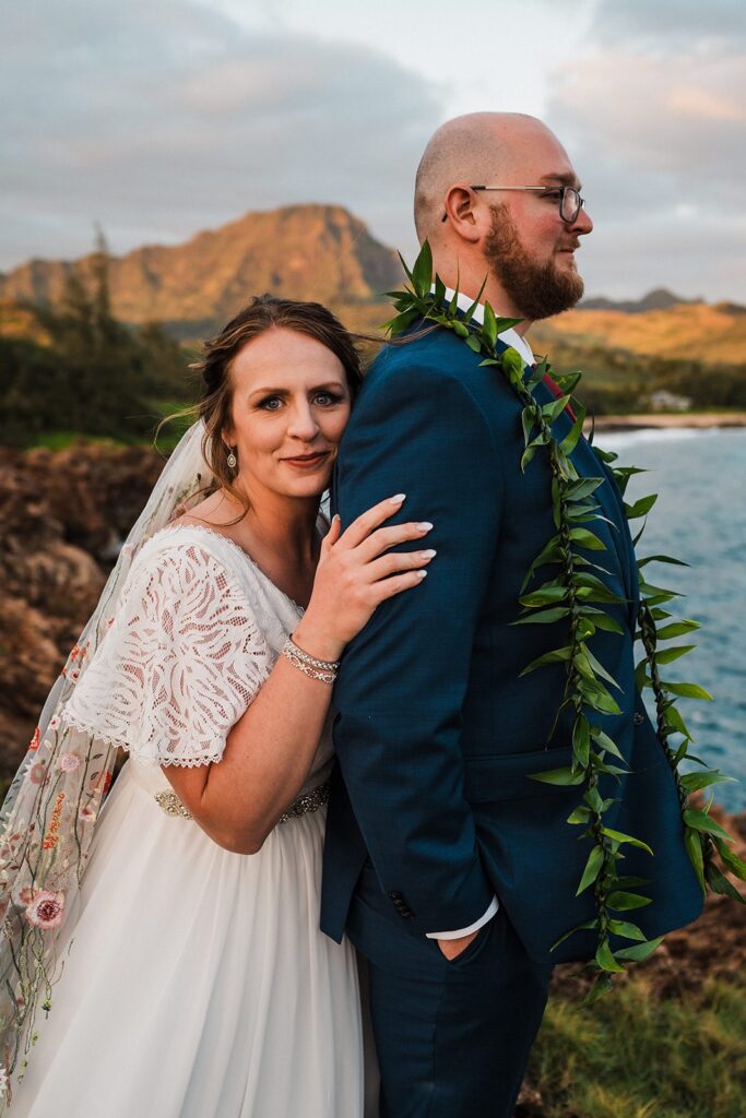 Bride leans her cheek against groom's shoulder during their sunset elopement photos in Kauai 