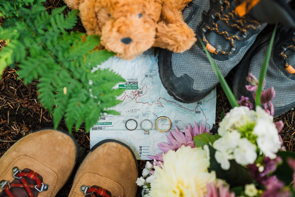 Stuffed bear, hiking boots, and Mount Rainier National park map with wedding bands detail shot 