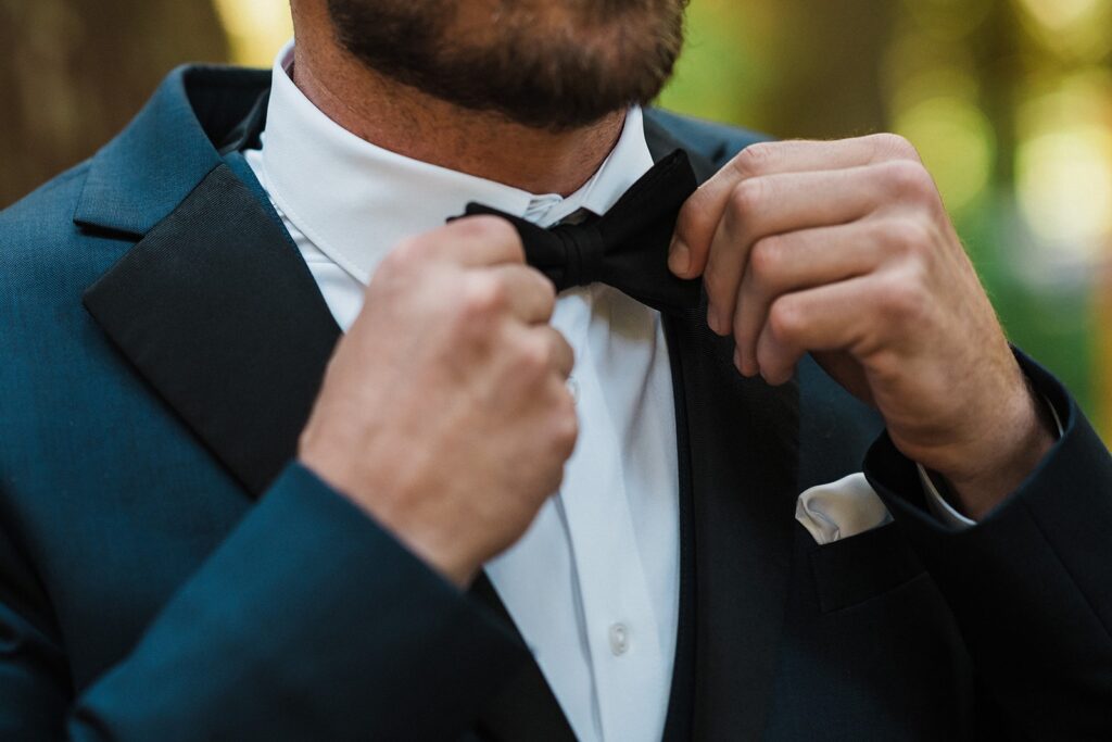 Groom adjusts black bow tie while getting ready for his Mount Rainier National Park elopement 