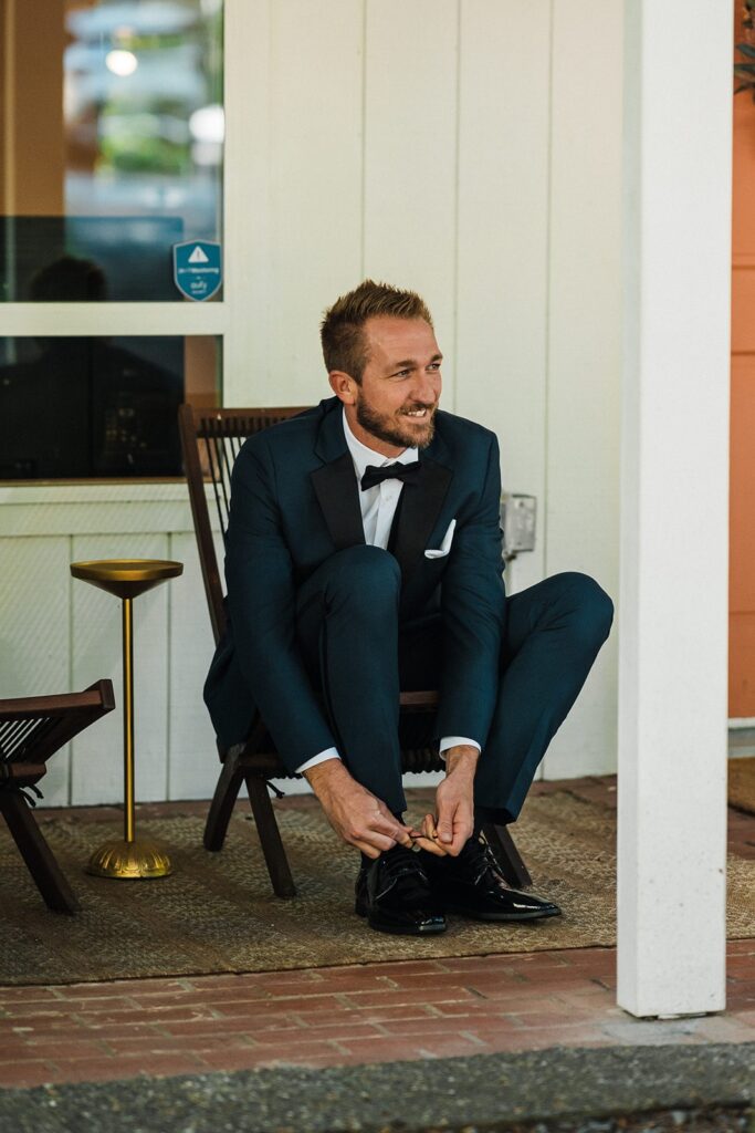 Groom laces up black dress shoes while getting ready for his elopement first look in Washington