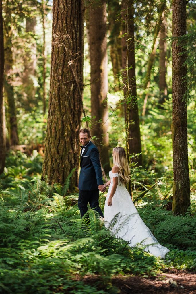 Bride and groom hold hands while walking through the forest during their Mount Rainier National Park elopement