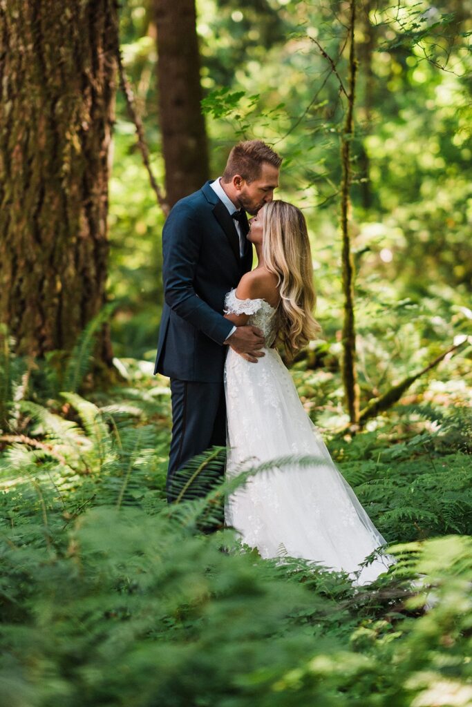 Groom kisses bride on the forehead during their forest adventure elopement in Mt Rainier National Park