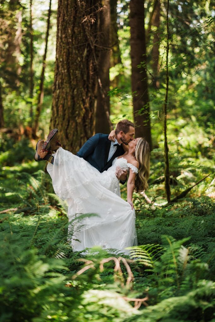 Groom dips bride for a kiss during their forest elopement photos at Mount Rainier National Park