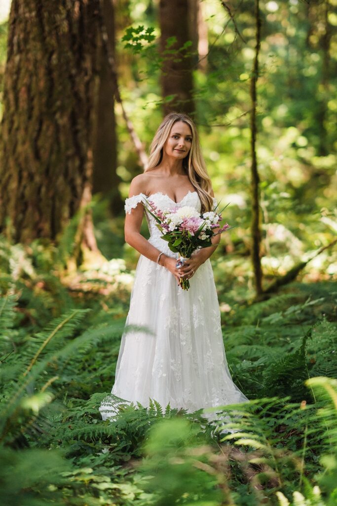 Bride holds pink and white elopement flower bouquet during wedding portraits in the forest 